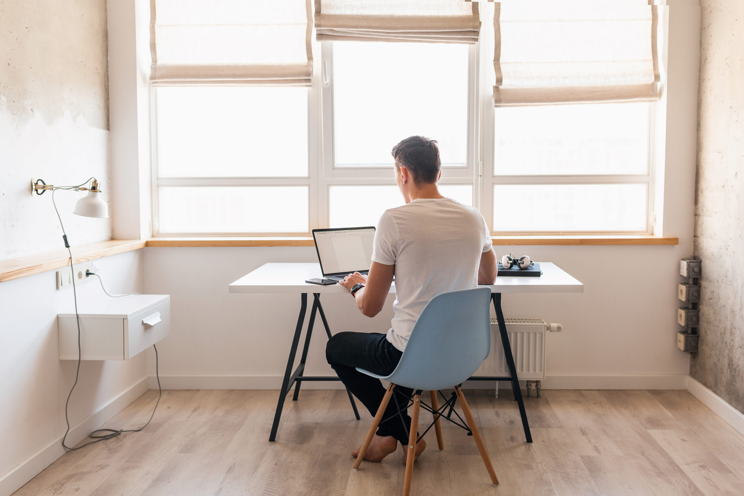young handsome man in casual outfit sitting at table working on laptop, freelancer at home, view from back
